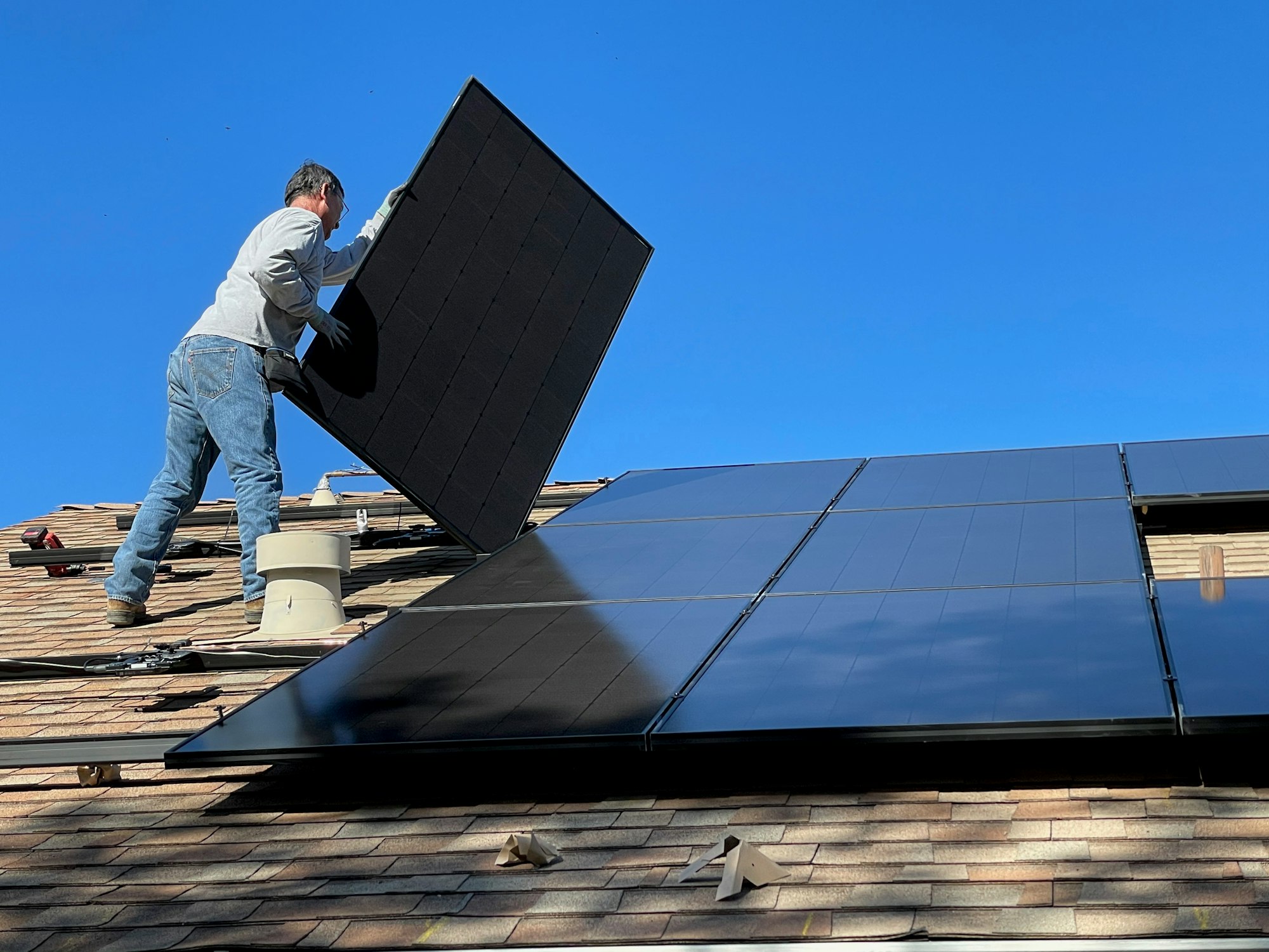 A worker lifting a solar module clear of a roof during a panel detach and reset